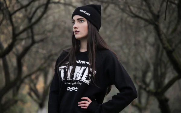 5K Ultra HD PC desktop wallpaper: black-haired woman model in a black beanie and sweatshirt, posing against a muted, leafless woodland background.