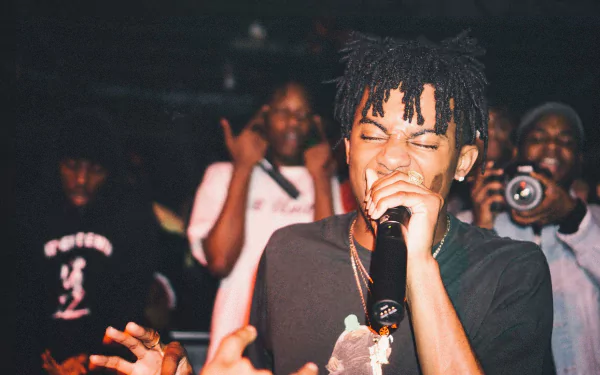 A vibrant HD wallpaper featuring Playboi Carti passionately performing on stage, surrounded by an engaged audience. The energetic atmosphere captures the essence of live music.