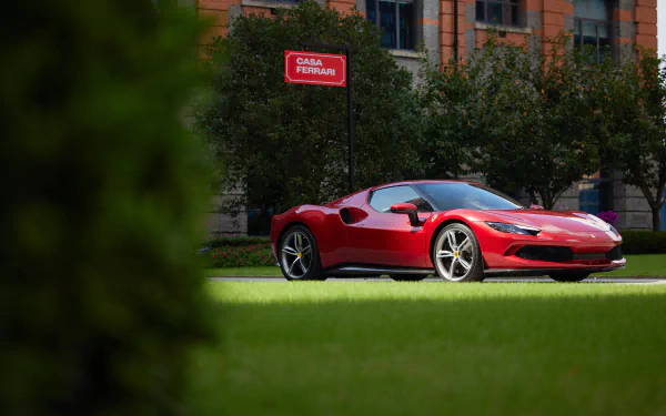Red Ferrari 296 GTB supercar parked on lawn before an urban building, captured as an 8K Ultra HD PC desktop wallpaper/background.
