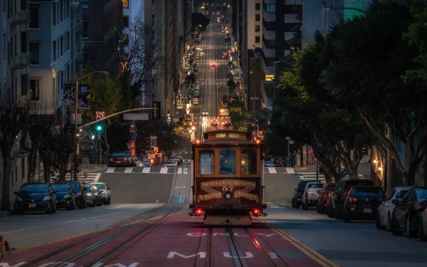 A vintage tram moves along a steep street in San Francisco, California, captured in stunning 4K Ultra HD, with city lights and parked cars lining the road.