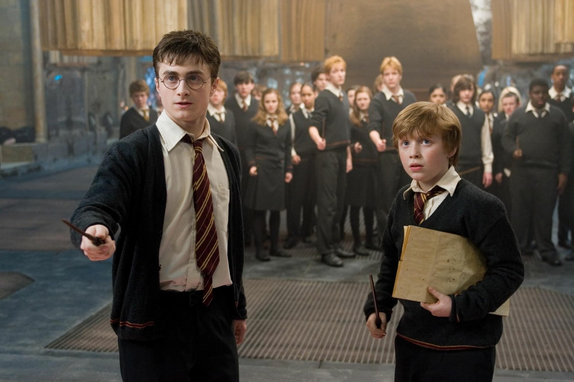 HD PC desktop wallpaper from Harry Potter and the Order of the Phoenix: Harry Potter in glasses points a wand while classmates in Hogwarts robes stand behind him.