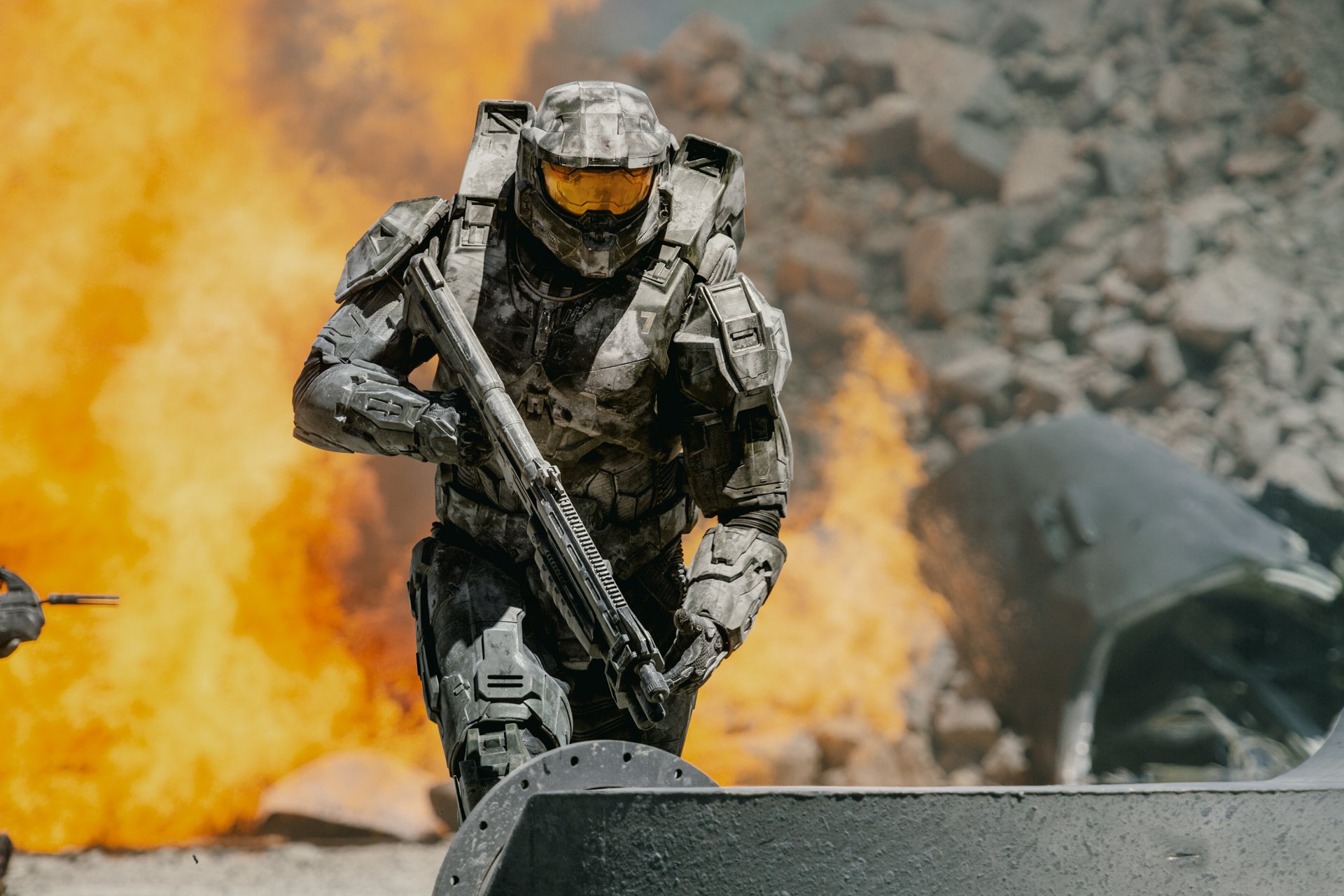 Master Chief from the Halo TV show in full armor, holding a weapon, with an intense fiery explosion in the background, captured in HD for a PC desktop wallpaper.