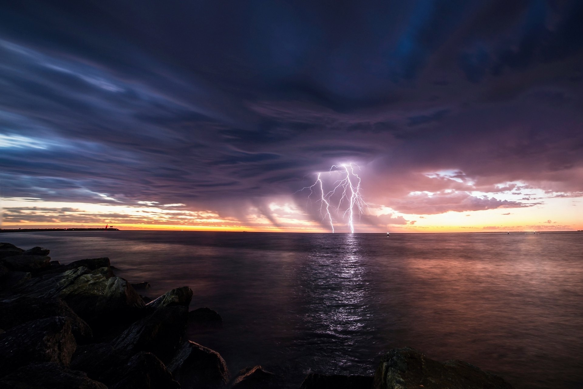 HD PC desktop wallpaper: horizon photography of a stormy sunset over the ocean with dramatic clouds and multiple lightning strikes reflecting on calm water.