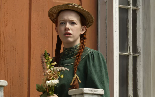 2K Quad HD PC desktop wallpaper: red‑haired girl in braids and green period dress holding flowers on a porch — scene from the TV show Anne with an E.