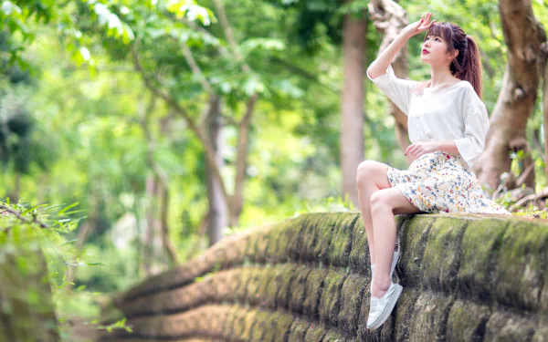 Asian woman in casual outfit sitting on a mossy stone wall surrounded by lush greenery, captured in vibrant detail for a 4K Ultra HD PC desktop wallpaper.