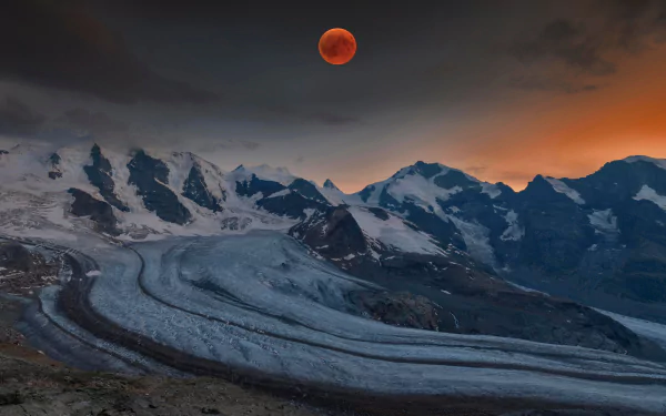 A dramatic blood moon lunar eclipse painting the night sky over the majestic Alps Mountain range in this HD nature desktop wallpaper.