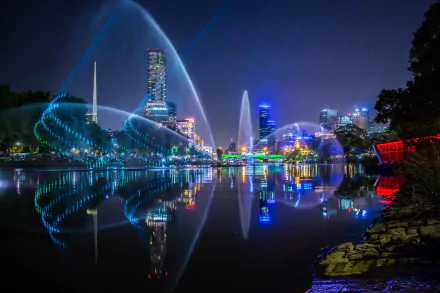 Nighttime view of Melbourne's city skyline and light reflections over calm water, showcasing vibrant man-made illumination and urban architecture.