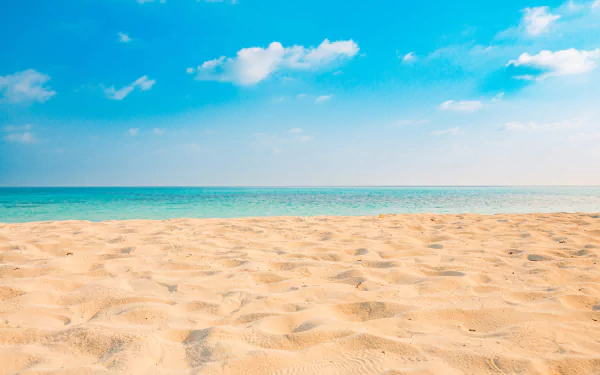 HD PC desktop wallpaper: sunlit rippled sand stretching to a turquoise sea under a clear blue sky with scattered white clouds.