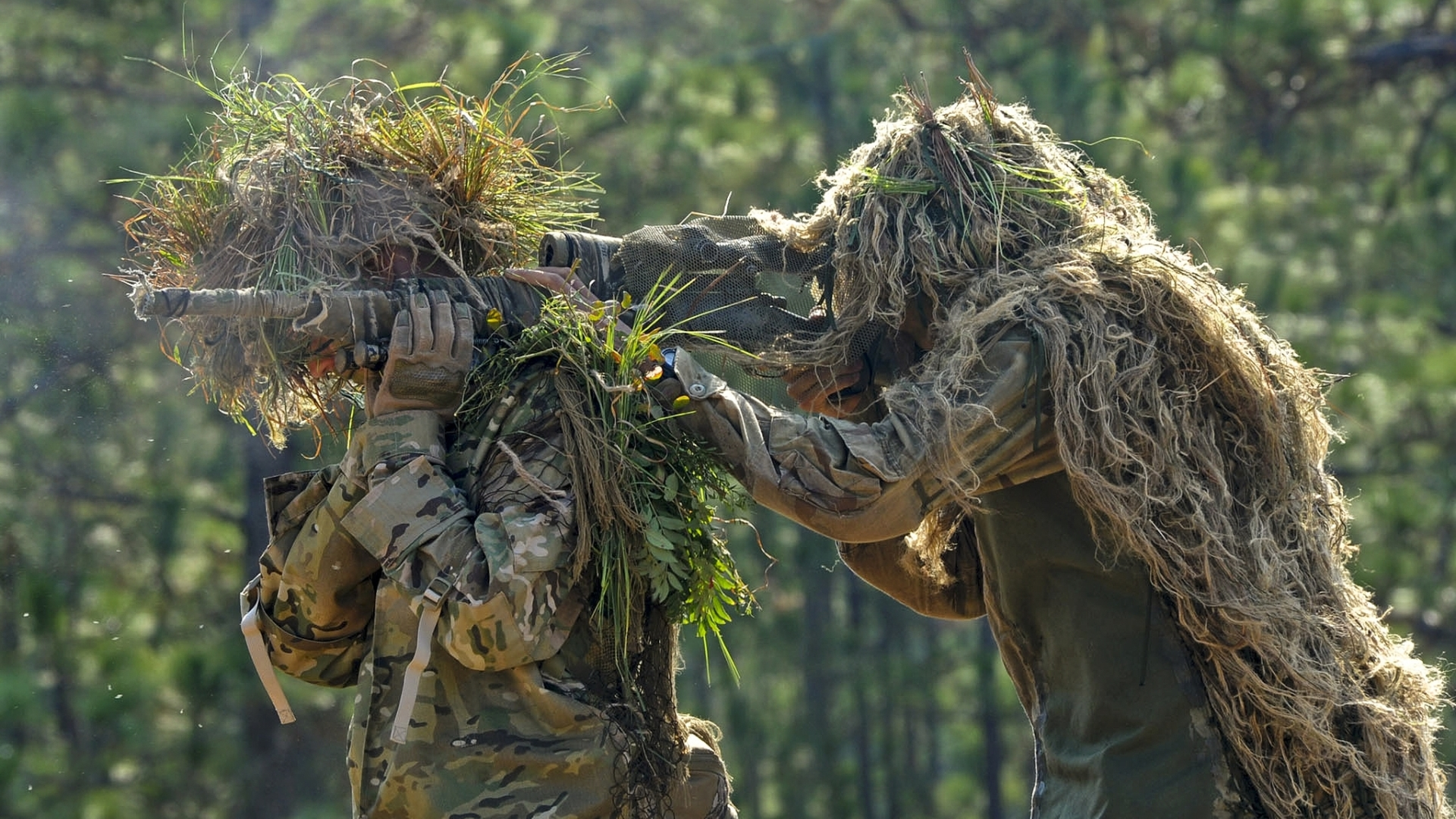 HD PC desktop wallpaper showing two military soldiers camouflaged with ghillie suits, aiming rifles as snipers in a forest setting.