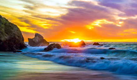 Vibrant sunset over a rocky shoreline with waves crashing, captured in 4K Ultra HD as a nature horizon desktop wallpaper.