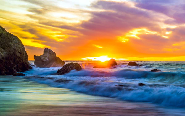 Vibrant sunset over a rocky shoreline with waves crashing, captured in 4K Ultra HD as a nature horizon desktop wallpaper.