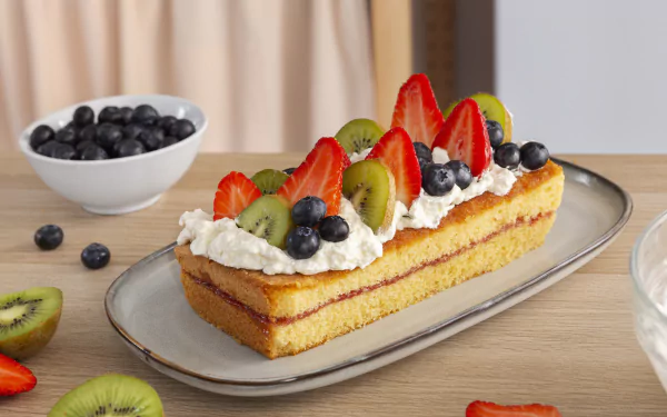 An 8K Ultra HD PC desktop wallpaper featuring a slice of layered cake topped with whipped cream, strawberries, kiwi, and blueberries on a gray plate.