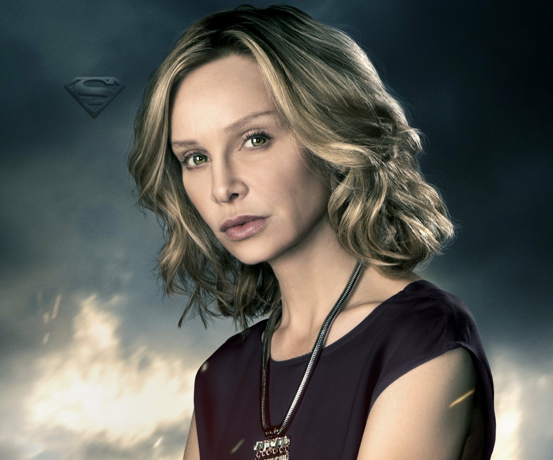 HD PC desktop wallpaper: close-up portrait of a woman from the TV show Supergirl, soft lighting and a faint S emblem in a smoky background.