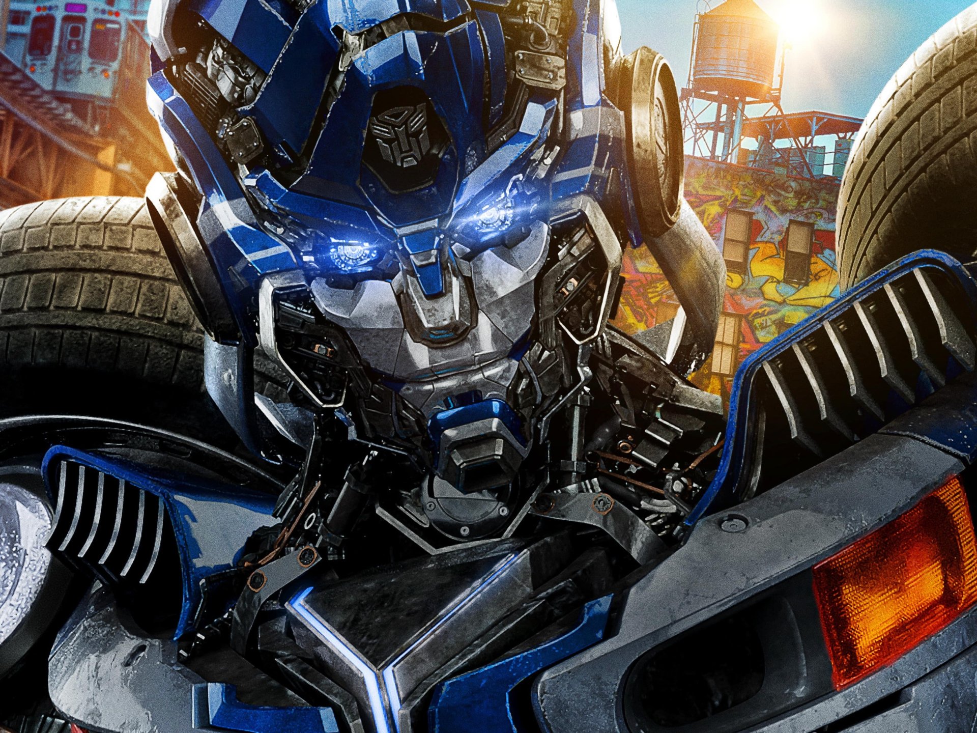HD PC desktop wallpaper featuring a close-up of a blue Transformer robot from the movie Transformers: Rise of the Beasts with vibrant urban background details.