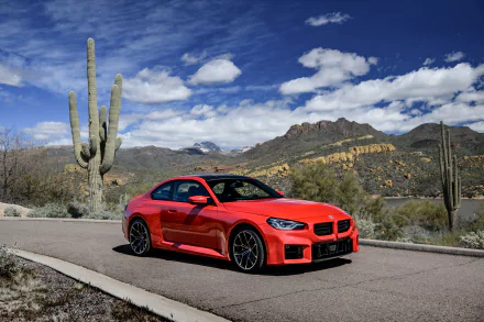Red BMW M2 on a desert road with saguaro cacti and rocky mountains beneath a bright blue sky — 8K Ultra HD PC desktop wallpaper and background.