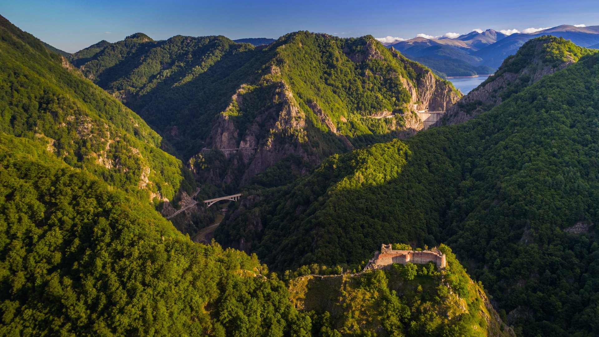 Aerial view of the man-made Poenari Castle nestled among lush, green mountains under a clear sky in this 4K Ultra HD PC desktop wallpaper.