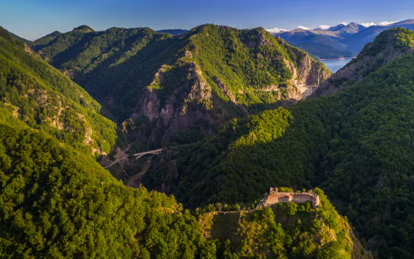 Aerial view of the man-made Poenari Castle nestled among lush, green mountains under a clear sky in this 4K Ultra HD PC desktop wallpaper.