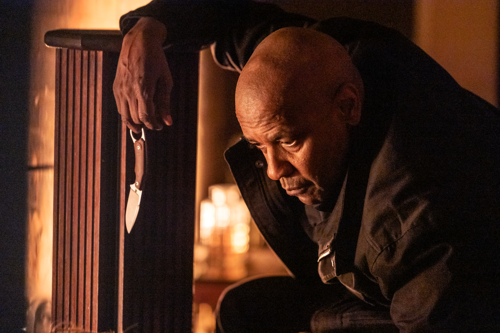 Denzel Washington in a tense moment from The Equalizer 3, featuring an intense close-up as he grips a knife, set against a dramatic background. HD desktop wallpaper.