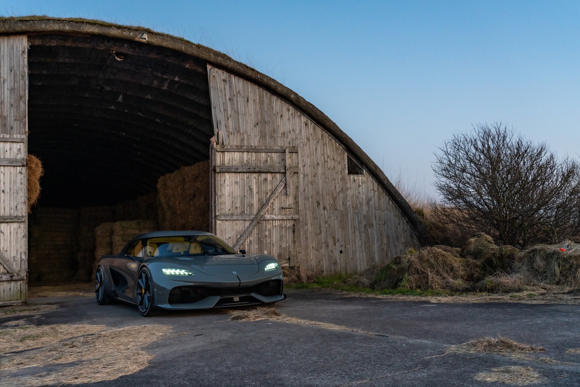 Koenigsegg Gemera parked outside a rustic barn at twilight, HD desktop wallpaper.