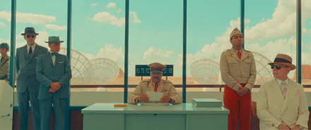 HD desktop wallpaper featuring a stylized scene from Asteroid City with three characters in uniform inside a room with large windows overlooking a desert landscape.