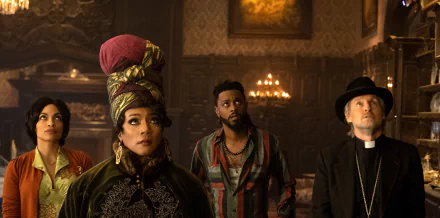 HD desktop wallpaper from the movie Haunted Mansion featuring four characters in an ornate room, dressed in thematic costumes, looking intently off-camera.