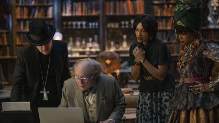 HD desktop wallpaper from the movie Haunted Mansion featuring four characters intently looking at a laptop in a library setting.