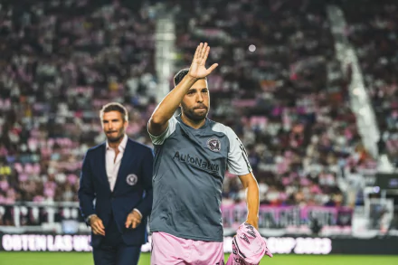 HD desktop wallpaper featuring Jordi Alba of Inter Miami CF waving on the field in a gray and pink uniform, with a blurred coach in the background.