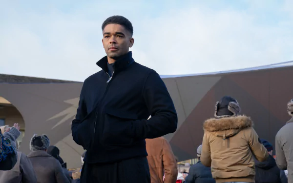 A character from the TV show Secret Invasion stands confidently in front of a modern structure, surrounded by a crowd, set against a cloudy sky. HD desktop wallpaper.