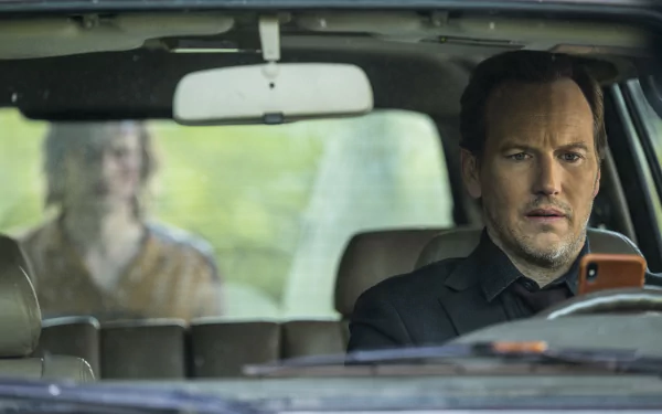 HD desktop wallpaper featuring a scene from Insidious: The Red Door with a man in the foreground looking intently at a phone while driving, and a blurred woman in the background.