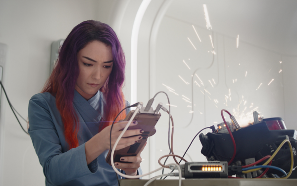 A woman with purple hair focused on operating a device with sparking machinery in the background, inspired by Ahsoka and Sabine Wren themes, in a high-definition desktop wallpaper.