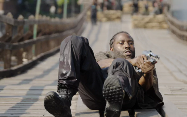 HD desktop wallpaper featuring a person lying on a wooden bridge with a determined expression, holding a gun, from 'The Creator' (2023).