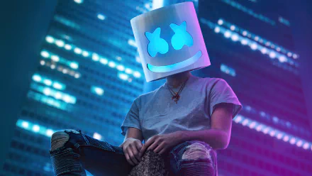 Person wearing a Marshmello head mask sitting in an urban setting at night with city lights in the background, for HD desktop wallpaper.