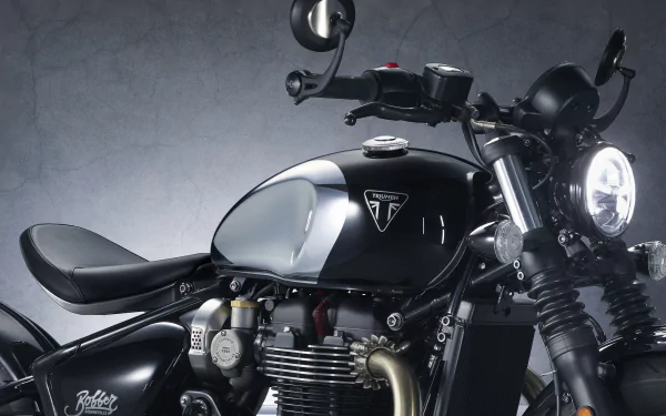 A close-up of a Triumph Bonneville Bobber Chrome Edition motorcycle, showcasing its sleek black design and modern features against a textured gray background.
