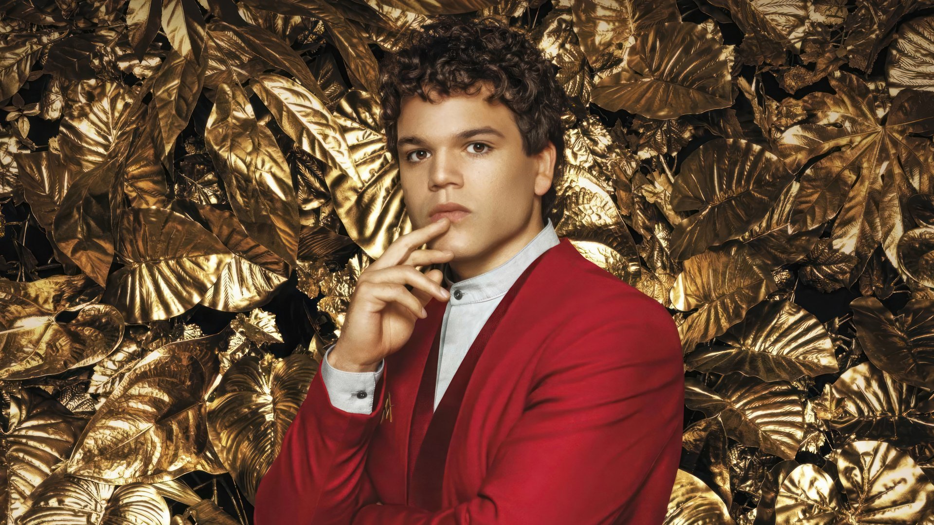 A contemplative individual in a red suit set against a golden foliage background themed around The Hunger Games: The Ballad of Songbirds & Snakes for HD desktop wallpaper.