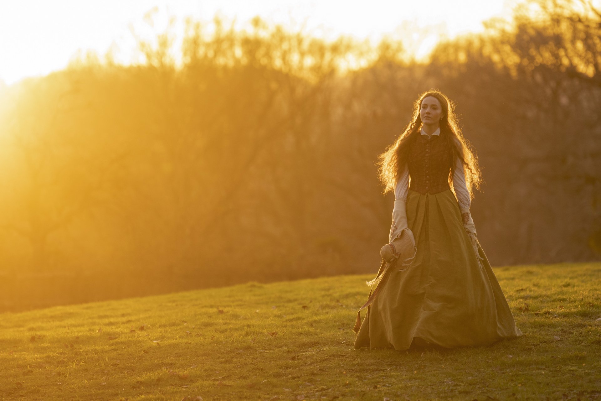 A character from the TV show Belgravia: The Next Chapter stands in a sunlit field, wearing a flowing gown, capturing a moment of tranquility at sunset. HD desktop wallpaper.