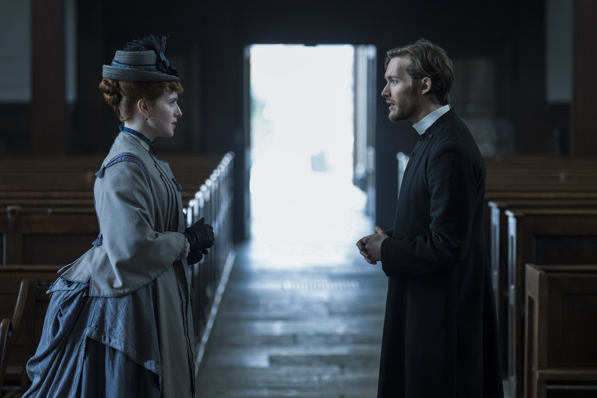 HD desktop wallpaper featuring two characters from Belgravia: The Next Chapter standing in a dimly lit church aisle, symbolizing drama and period intrigue.