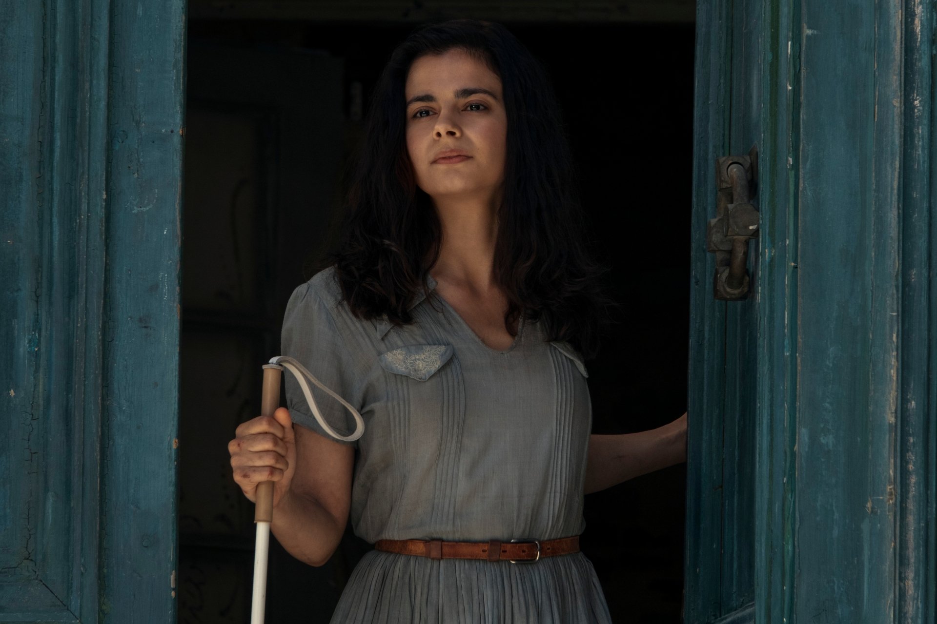 HD wallpaper featuring a scene from the TV show 'All the Light We Cannot See' with a woman holding a cane, standing in a doorway.