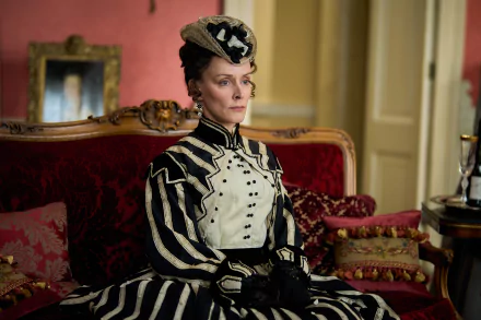 Elegant character from Belgravia: The Next Chapter dressed in Victorian attire sitting on an antique sofa with luxurious red background – HD desktop wallpaper.