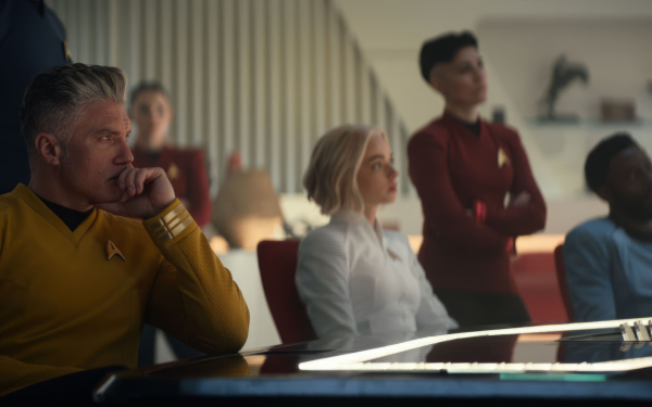 HD wallpaper featuring characters from Star Trek: Strange New Worlds, with a focus on a male officer in a yellow uniform thoughtfully seated at the forefront.