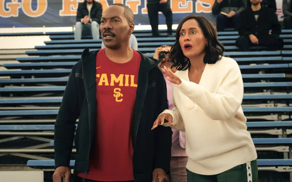 A scene from the movie Candy Cane Lane, featuring two characters on bleachers, displaying excitement and concern, set against a vibrant sports backdrop. HD desktop wallpaper.