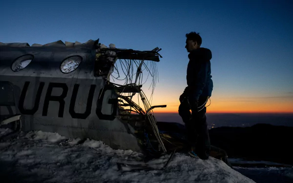 A person standing beside a wrecked airplane with the word 'URUG' at dusk - HD wallpaper inspired by the movie Society of the Snow.