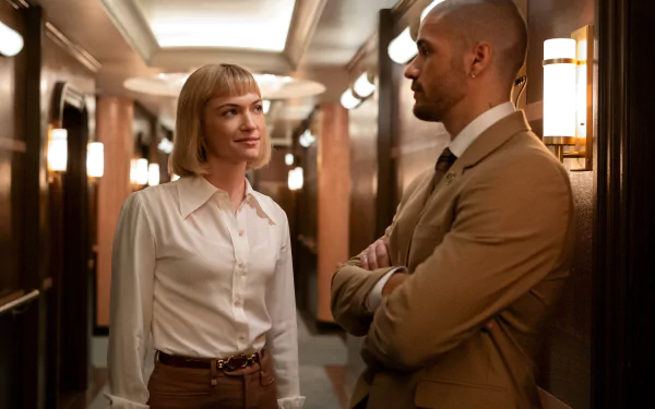 A captivating scene from the TV show Death and Other Details, featuring two characters engaged in conversation in a stylishly lit hotel hallway.