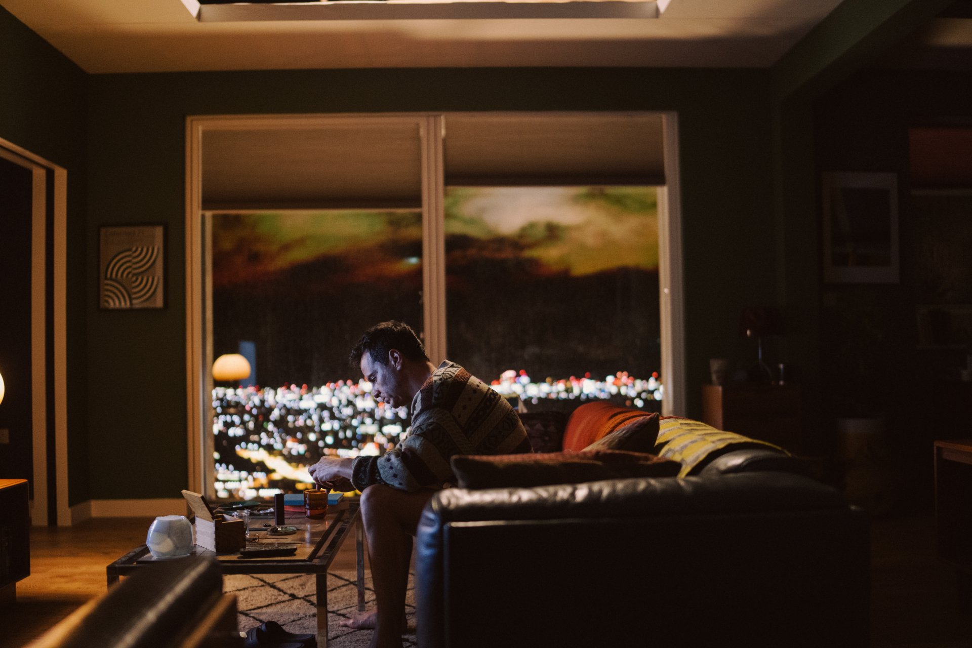 HD wallpaper featuring a contemplative scene from All of Us Are Strangers with a person sitting by the window overlooking city lights.