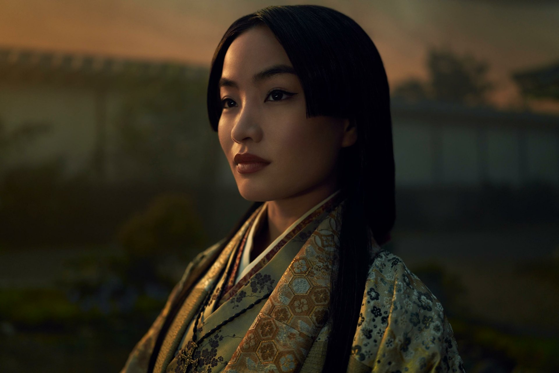 HD desktop wallpaper featuring a character from Shogun (2024) TV show, adorned in traditional attire with a serene expression and a dusk backdrop.
