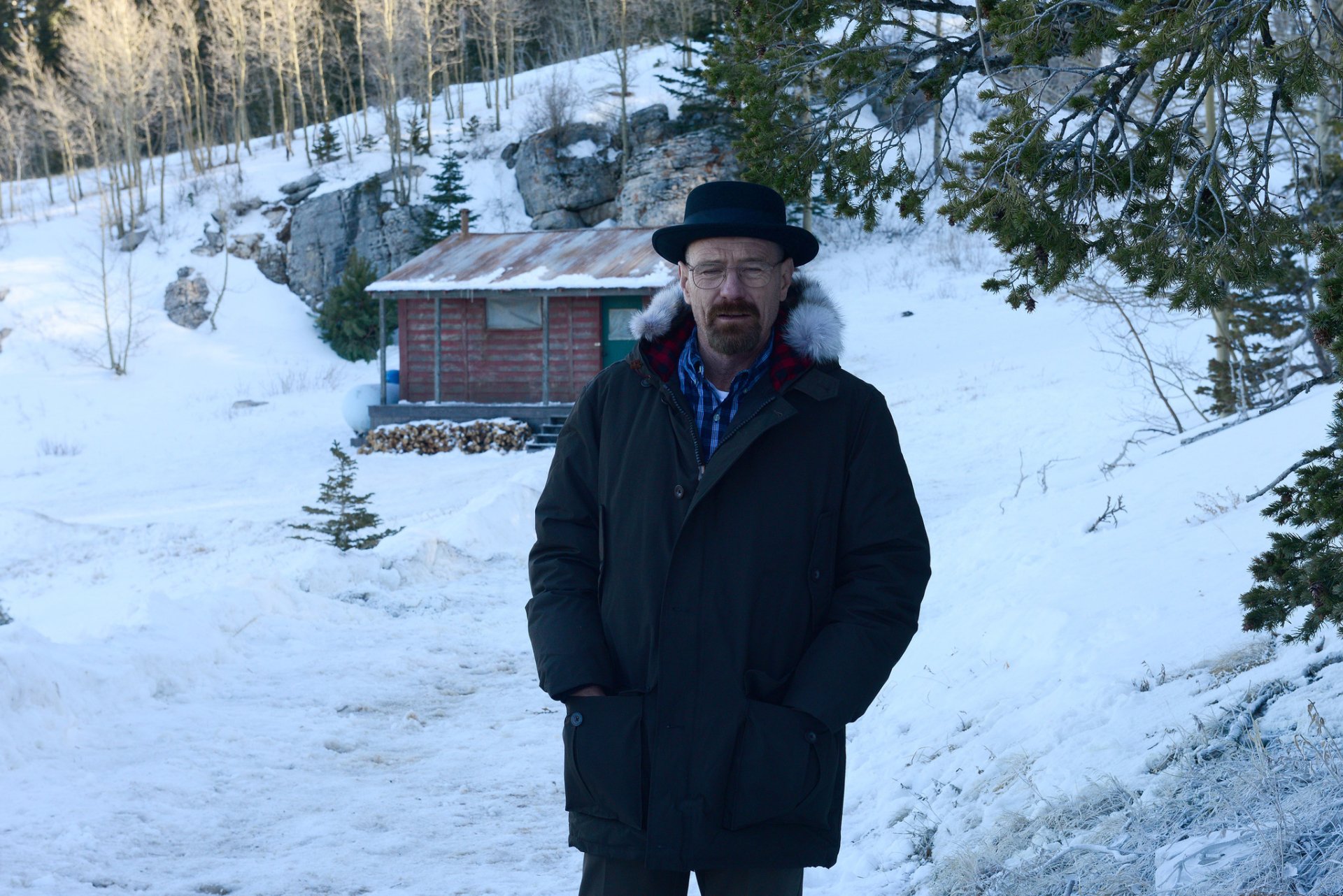 High-definition desktop wallpaper featuring a man resembling Walter White from the TV show Breaking Bad, standing in a snowy landscape with a small cabin in the background.