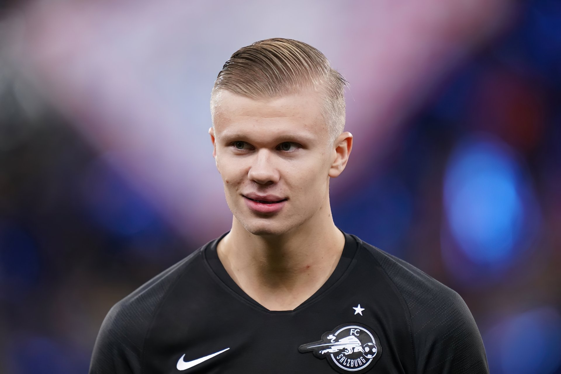 Professional soccer player in a black sports kit against a blurred stadium background, featured in a high-definition desktop wallpaper.