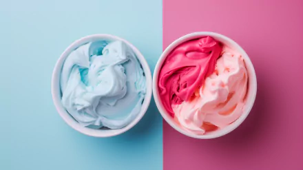 Two bowls of colorful frozen yogurt, one blue and one pink, sit against a split background of light blue and pink, creating a vibrant and appetizing dessert scene.