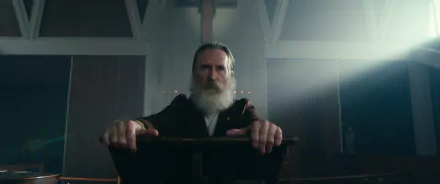 HD wallpaper featuring a scene from the TV Show 'The Gentlemen (2024)' with a distinguished bearded man seated and leaning forward in a solemn, dimly lit setting.