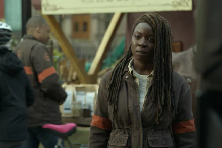 Danai Gurira as Michonne from The Walking Dead: The Ones Who Live stands focused in a bustling scene, embodying resilience amidst chaos. A striking HD wallpaper for fans.