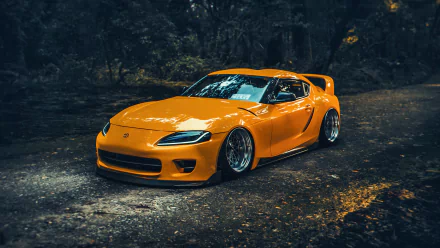 A striking orange Toyota Supra A90 parked on a winding road, surrounded by lush greenery, capturing the essence of speed and style in this HD desktop wallpaper.